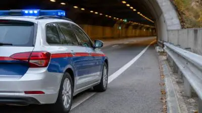 KI-generiertes Bild: Ein blau-weißes Auto mit Blaulicht steht in einem Straßentunnel neben einer Leitplanke.