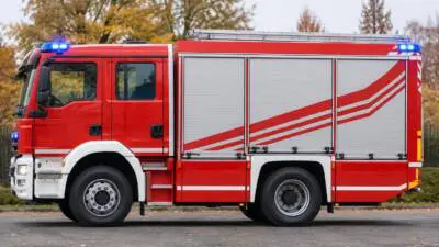 KI-generiertes Bild: Ein rotes Löschfahrzeug mit eingeschaltetem Blaulicht steht vor Bäumen.