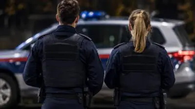 KI-Symbolbild: Uniformierte Personen vor einem weiß-blauen Fahrzeug mit blauem Signallicht.