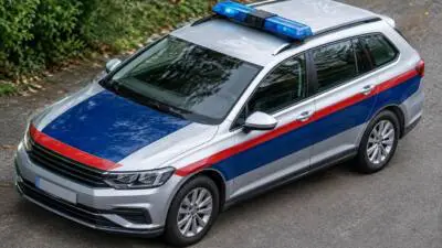 KI-generiertes Bild: Ein silberner Kombi mit blauem Warnlicht und farbigen Streifen steht auf einer Straße.