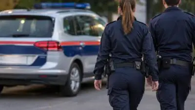 KI-Symbolbild: Uniformierte Personen gehen auf ein weißes Auto mit Blaulicht zu.