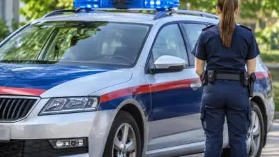 KI-Symbolbild: Eine uniformierte Person steht neben einem weiß-blau-roten Auto mit Blaulicht.