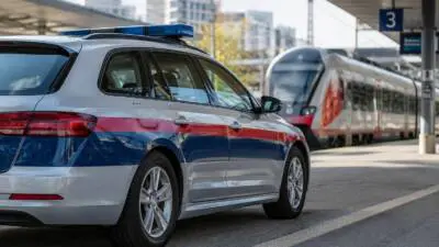 KI-Symbolbild: Ein silberner Kombi mit blau-rotem Streifen und Blaulicht steht neben einem Zug am Bahnsteig.