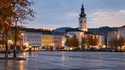 KI-generiertes Bild: Beleuchtete Gebäude mit Turm an einem gepflasterten Platz bei Dämmerung.