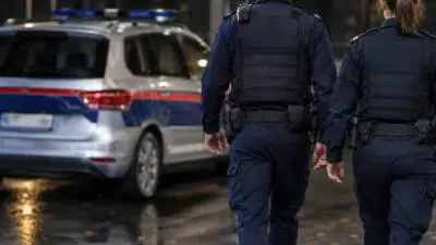KI-Symbolbild: Uniformierte Personen neben einem silbernen Einsatzfahrzeug auf nasser Straße.