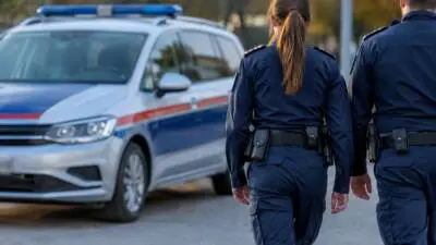 KI-Symbolbild: Uniformierte Personen gehen neben einem blau-weißen Auto mit Blaulichtbalken.