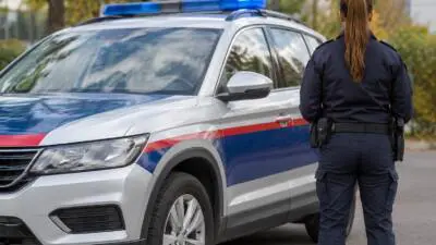 KI-Symbolbild: Eine uniformierte Person steht neben einem weiß-blauen Fahrzeug mit Blaulicht.
