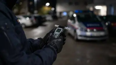 KI-Symbolbild: Eine Person hält ein Atemalkoholmessgerät vor unscharfen Fahrzeugen.