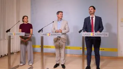 Drei Personen stehen an Rednerpulten vor einer Kulisse des Landes Kärnten.