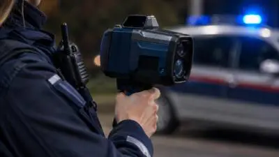 KI-generiertes Bild: Eine uniformierte Person hält ein Messgerät neben einem unscharfen Auto mit blauem Licht.