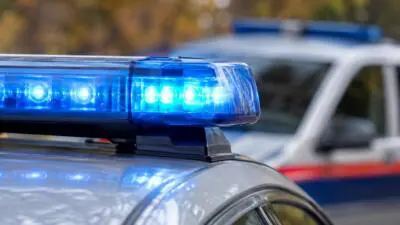 KI-Symbolbild: Ein blaues Warnlicht auf einem silbernen Auto, dahinter unscharfe Fahrzeuge.