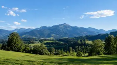 KI-Symbolbild: Grüne Wiesen und bewaldete Berge unter blauem Himmel mit lockeren Wolken.