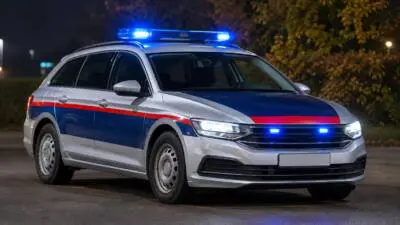 KI-generiertes Bild: Ein silberner Kombi mit blau-roter Gestaltung und blauem Blinklicht bei Nacht.