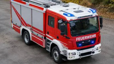 KI-generiertes Bild: Ein roter und weißer Feuerwehr-Lkw mit Leiter steht auf einer Straße.