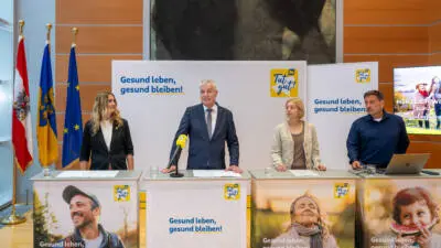Teilnehmende einer Pressekonferenz stehen hinter mit „Tut gut!“ beschrifteten Pulten.