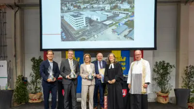 Gäste posieren bei der Eröffnung des neuen Amtsgebäudes und Wirtschaftshofs in Klosterneuburg vor einer Projektion mit einer Gebäudeanlage.