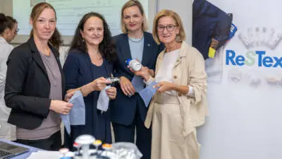 Frauen präsentieren Stoffproben vor einer ReSTex-Ausstellung zur Textilforschung.