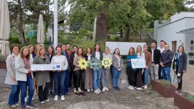 Eine Gruppe steht vor einem Gebäude und hält Schilder sowie farbige LEADER-Symbole in die Kamera.