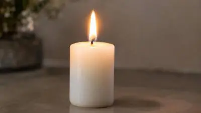 KI-generiertes Bild: Eine brennende weiße Stumpenkerze steht auf einer Tischfläche.