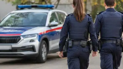 KI-Symbolbild: Uniformierte Personen vor einem blau-weiß-roten Fahrzeug mit Blaulicht.