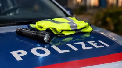 KI-generiertes Bild: Eine gelbe Warnweste und eine Taschenlampe liegen auf der Motorhaube eines Polizeiautos.