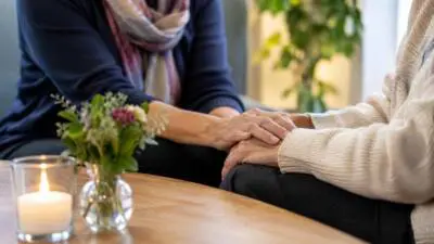 KI-Symbolbild: Eine Person legt einer anderen am Tisch die Hand auf.