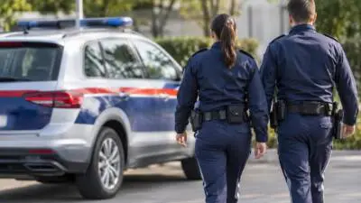 Uniformierte Personen gehen neben einem blau-weißen Fahrzeug mit Blaulichtbalken.
