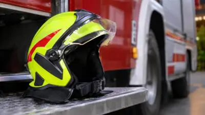 KI-Symbolbild: Ein gelber Schutzhelm liegt auf der Trittfläche eines roten Einsatzfahrzeugs.