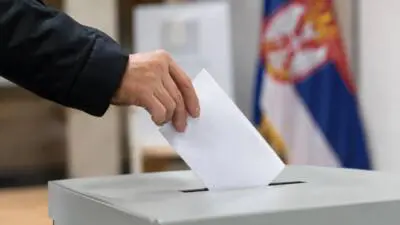 KI-Symbolbild: Eine Hand steckt einen weißen Stimmzettel in eine graue Wahlurne.