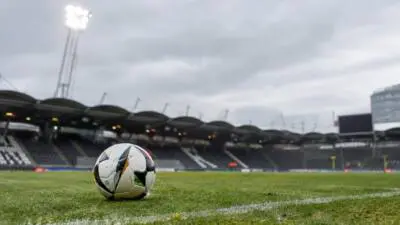KI-Symbolbild: Ein Fußball liegt auf dem Rasen vor leeren Stadiontribünen.