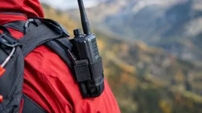 KI-Symbolbild: Eine rote Outdoorjacke mit Rucksack und Funkgerät vor einer Berglandschaft.