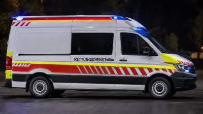 KI-generiertes Bild: Ein weißer Rettungsdienstwagen mit eingeschaltetem Blaulicht steht auf einer dunklen Straße.