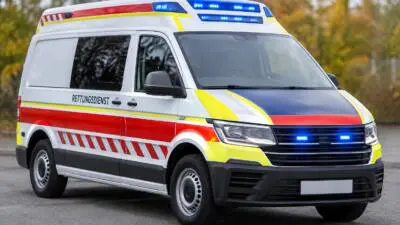 KI-generiertes Bild: Ein weißer Rettungswagen mit roten und gelben Streifen und eingeschaltetem Blaulicht.