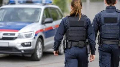 KI-generiertes Bild: Dunkelblau uniformierte Personen gehen neben einem weiß-blauen Wagen mit Blaulicht.