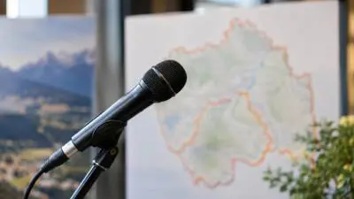 KI-Symbolbild: Ein schwarzes Mikrofon steht vor einer unscharfen Karte und alpinen Landschaft.