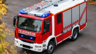 KI-generiertes Bild: Ein rotes Einsatzfahrzeug mit Leiter steht auf einer asphaltierten Fläche.