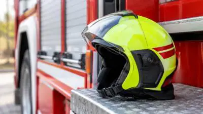KI-Symbolbild: Ein leuchtgelber Schutzhelm liegt auf einer silbernen Trittstufe vor einem roten Fahrzeug.