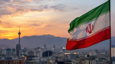 KI-Symbolbild: Eine iranische Flagge weht vor einer Stadt- und Bergsilhouette im Abendlicht.