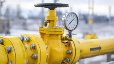 KI-generiertes Bild: Gelbe Rohrleitung mit Ventil und Manometer vor unscharfer Industrieanlage.