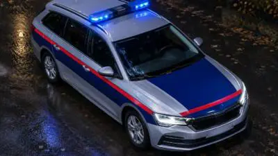 KI-Symbolbild: Ein silberner Kombi mit rot-blauer Markierung und Blaulicht auf nasser Straße.