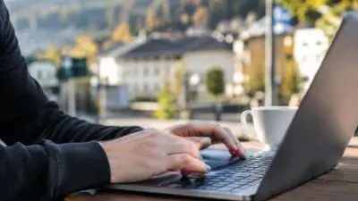 KI-generiertes Bild: Hände tippen an einem Laptop auf einem Tisch vor unscharfer Bergkulisse.