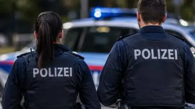KI-generiertes Bild: Polizeikräfte in dunklen Westen vor einem Streifenwagen mit blauem Licht.