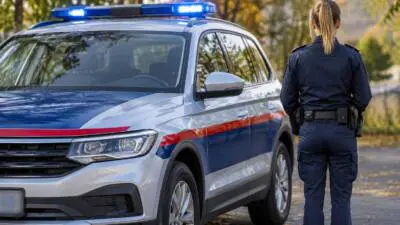 KI-Symbolbild: Eine uniformierte Person steht neben einem weiß-blauen Fahrzeug mit Blaulicht.