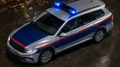 KI-Symbolbild: Ein silberner Kombi mit blau-roter Gestaltung und Blaulicht steht auf nasser Straße.