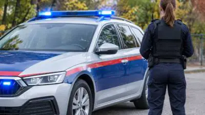 KI-generiertes Bild: Eine Person in dunkler Uniform steht neben einem silbernen Auto mit blau-roten Streifen und Blaulicht.