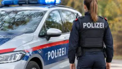 KI-generiertes Bild: Eine Polizistin steht neben einem Polizeiauto mit eingeschaltetem Blaulicht.