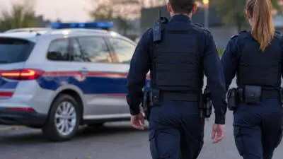 KI-Symbolbild: Uniformierte stehen neben einem weiß-blauen Fahrzeug mit Blaulicht.