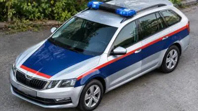 Silberner Kombi mit blau-roten Streifen und Blaulicht steht auf einer Straße.