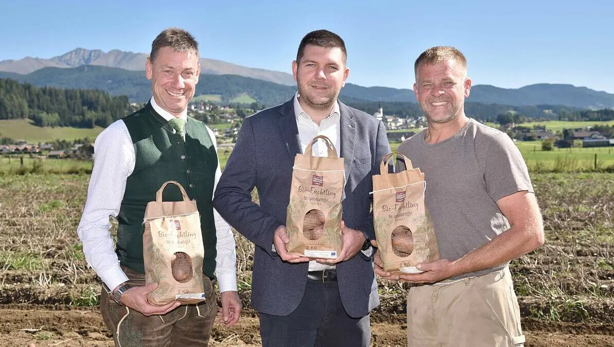 Drei Männer präsentieren Säcke mit Bio-Eachtling auf einem Feld; SPAR bietet die Lungauer Bio-Kartoffeln wieder an.