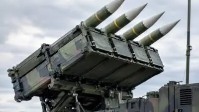 KI-generiertes Bild: Ein getarnter Raketenwerfer mit aufgerichteten Flugkörpern vor bewölktem Himmel.